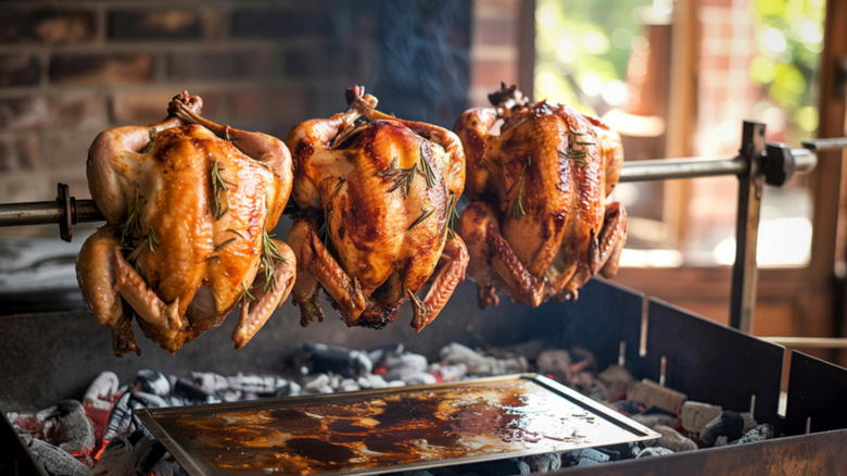 Three cooking rotisserie chickens on a spit