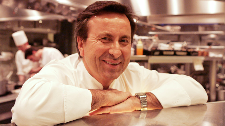 Daniel Boulud leaning on a metal counter in a restaurant kitchen