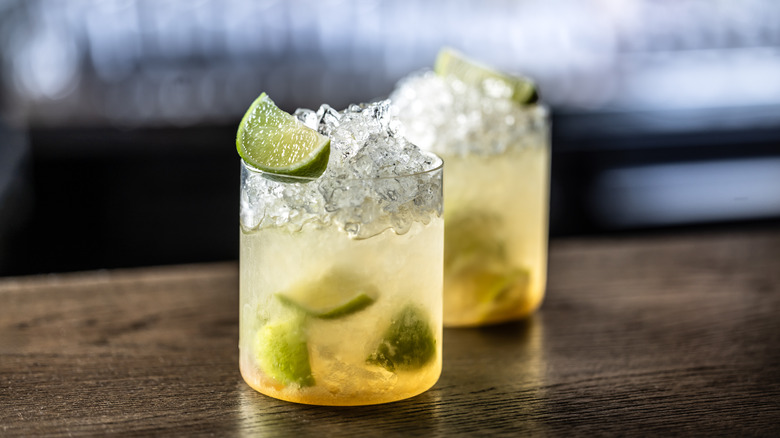 Two caipirinhas in rocks glasses on a wooden table.