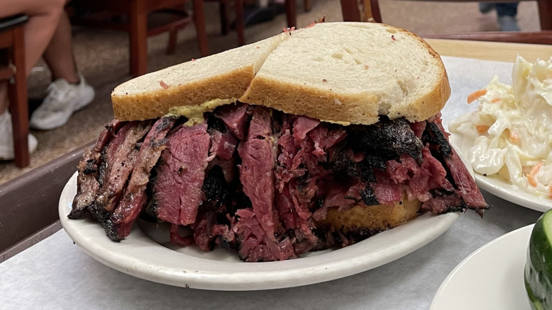 A heaping pastrami sandwich with sides of coleslaw and pickles on a table at Katz's deli