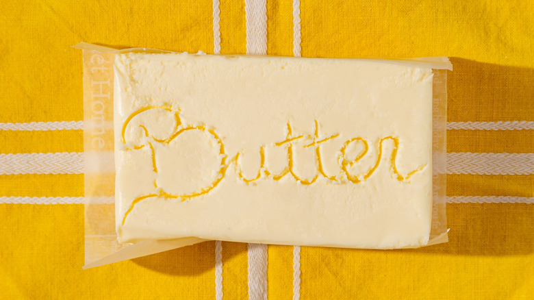Block of plastic wrapped butter on yellow tablecloth.