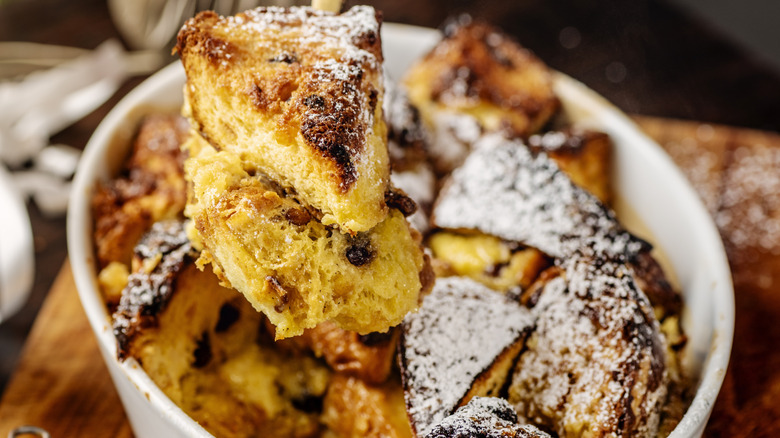 Close up of bread pudding pieces over bowl of bread pudding.