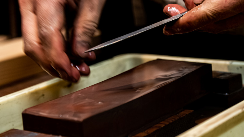 A hand sharpening a blade with a whetstone