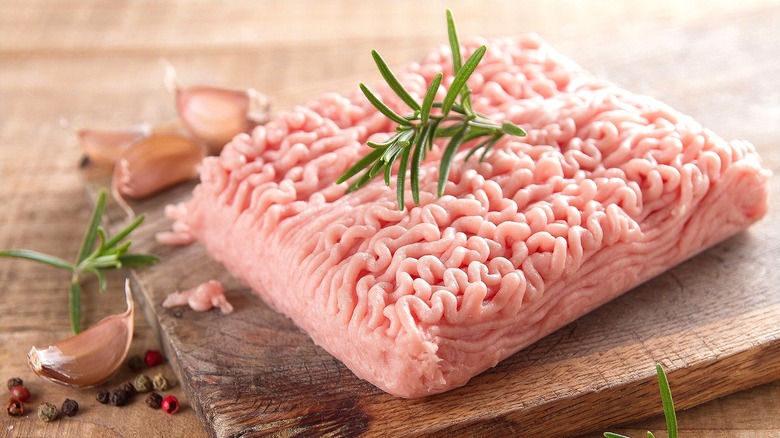 Raw ground turkey with fresh rosemary and garlic cloves on a wooden cutting board