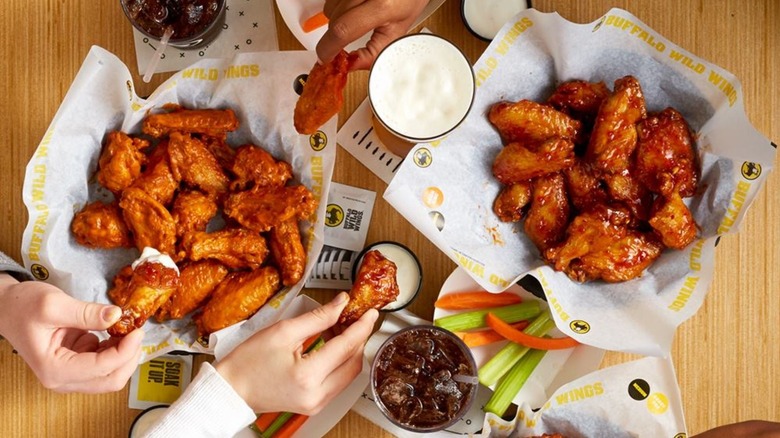 Top-down view of people's hands picking up and dipping an assortment of chicken wings at Buffalo Wild Wings