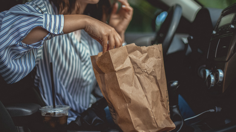 Woman reaches into bag of fast food in her car