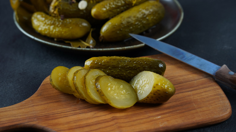 Pickles are chopped on a cutting board with more whole pickles in a bowl in the background.