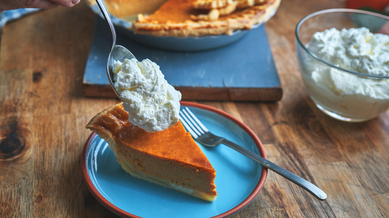 A slice of cake on a blue plate being topped with whipped cream using a spoon