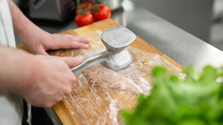 A person's hands are seen pounding chicken with a mallet.
