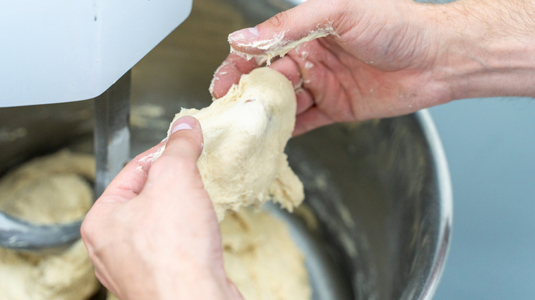 hands holding sticky bread dough over a stand mixer