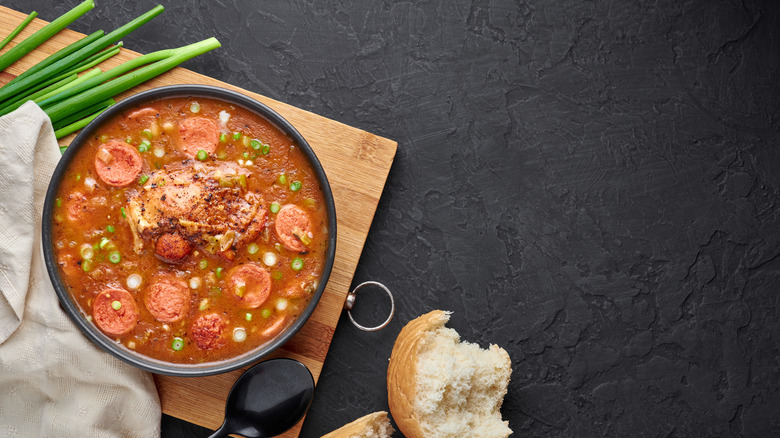 A meaty gumbo in a bowl placed on a wooden board against a black background