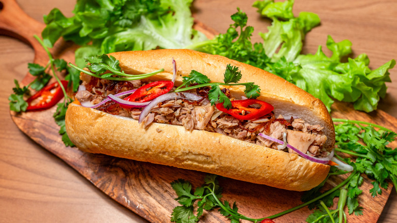Banh mi sandwich on a bed of greens and a cutting board.