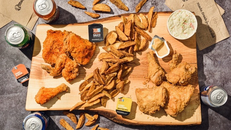 top down view of spread of fried chicken and potato wedges with Mary Brown's branded sauce packets and soda cans