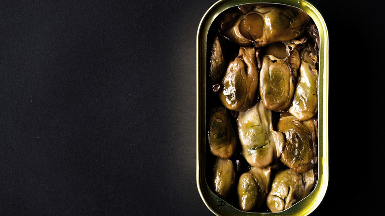 An open tin of smoked, canned oysters on a black countertop.