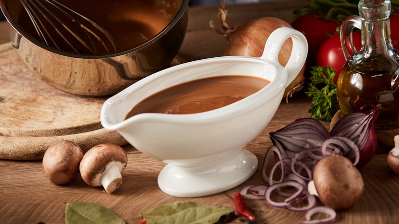Gravy in a white ceramic gravy boat next to vegetables on a wooden board
