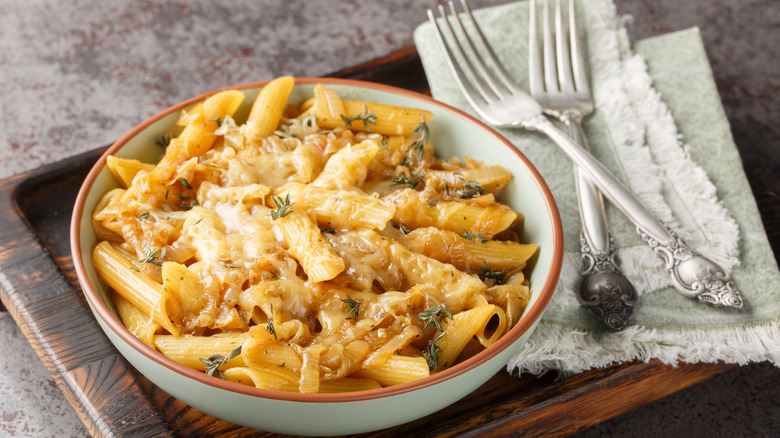 A bowl of French onion soup pasta on a wooden board.
