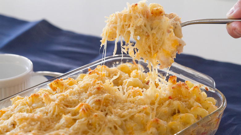Hand scooping baked macaroni and cheese out of a glass dish