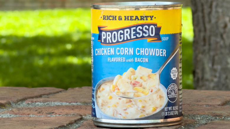A can of Progresso Chicken Corn Chowder flavored with bacon outside on a red brick surface