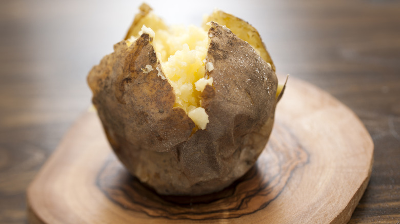 A baked potato split open on a wooden board