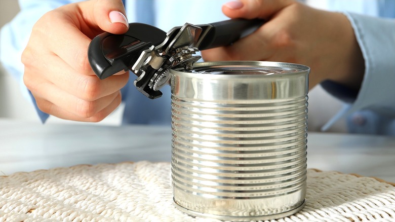 Hands opening a can of food with a manual can opener