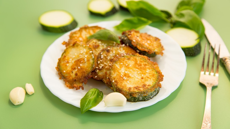 Crispy zucchini in a plate with garlic and sesame seeds on green background