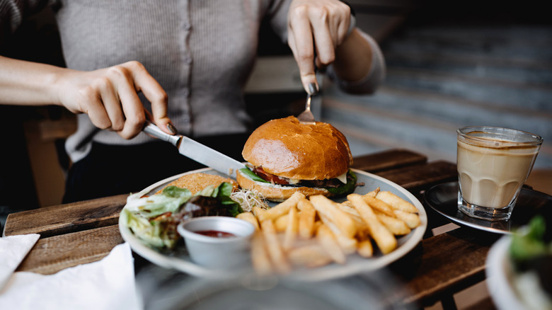 A person digs into a big burger with a knife and fork.