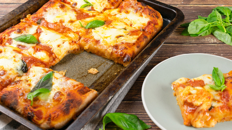 A slice is removed to a plate from a cheesy sheet pan pizza.