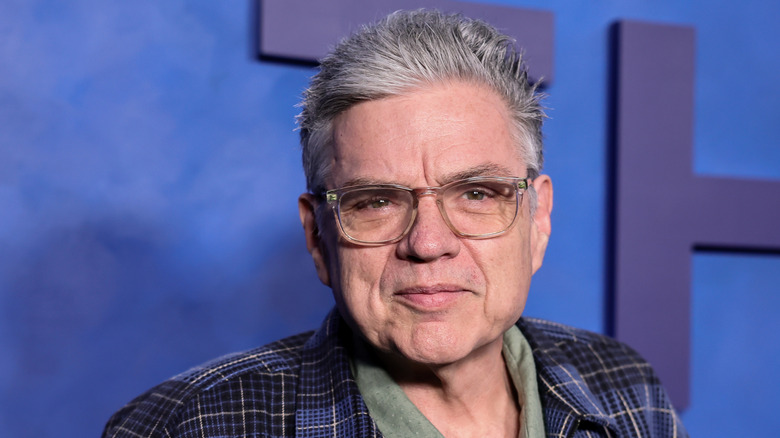 Actor Oliver Platt stands in front of a blue wall.