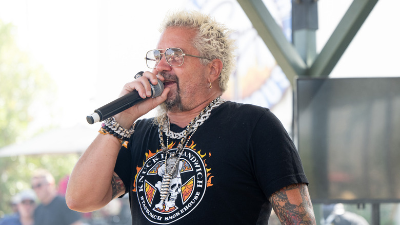 Celebrity chef Guy Fieri speaks into a microphone on stage at an event