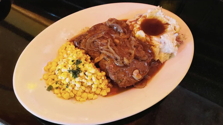 A plate of meatloaf with onions, mashed potatoes, gravy, and corn on the side.