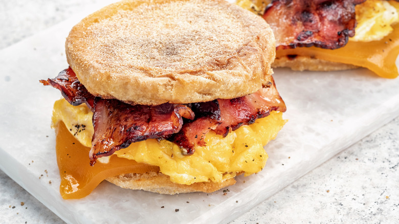 English muffin, scrumbled egg, ham, and cheese breakfast sandwich on a cutting board