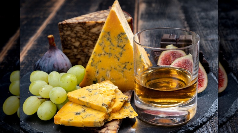 A glass of whiskey with a plate of cheese and fruits