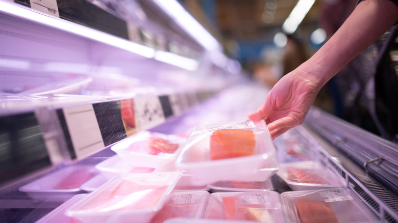Hand taking a packaged fish filet from a grocery store display