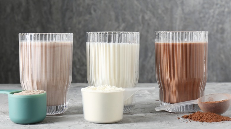 Three flavors of protein shakes sit on a table with protein powder
