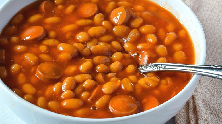 Close-up of saucy franks and beans with a metal spoon in a white bowl