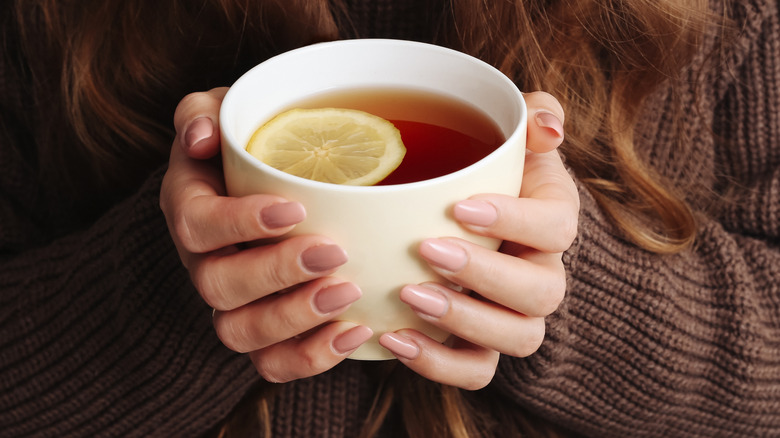 A pair of hands holding a cup of hot tea with lemon
