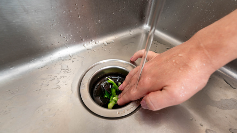Close up of hand putting food into garbage disposal