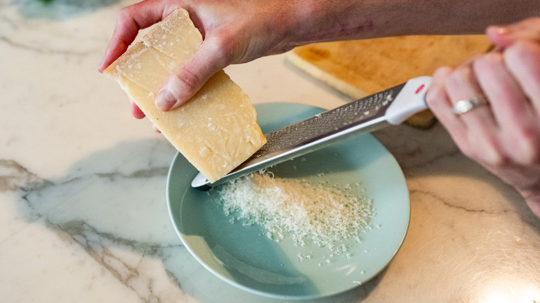 A person grating parmesan cheese onto a plate.
