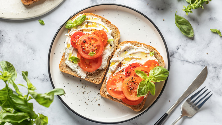Two slices of toast with cream cheese, tomatoes, and basil on a plate