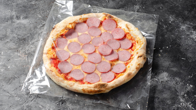 Frozen pepperoni pizza sitting on a piece of plastic and countertop