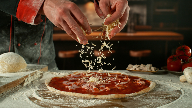 Freeze motion of pizza maker's hands drizzling cheese onto pizza dough