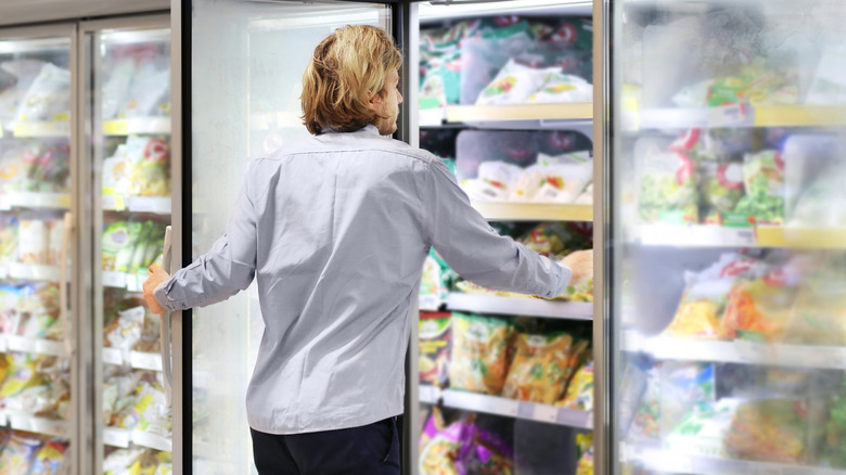 Person reaching into a freezer in a grocery store frozen foods aisle