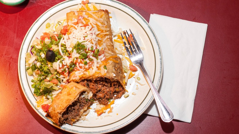 plate with a chimichanga covered in cheese, fork on the side