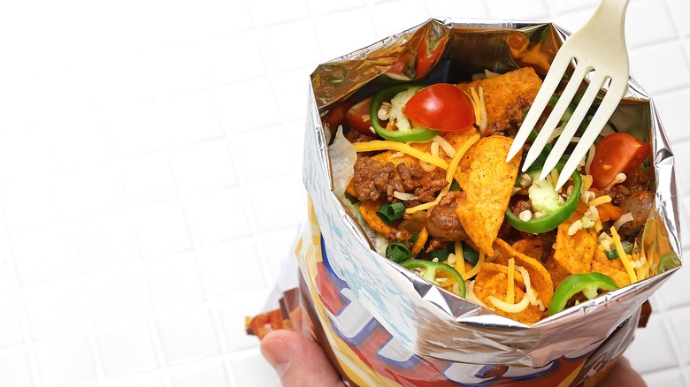 Hand holding a bag of Fritos filled with ground beef, diced cherry tomatoes, fresh jalapeños, and shredded cheese