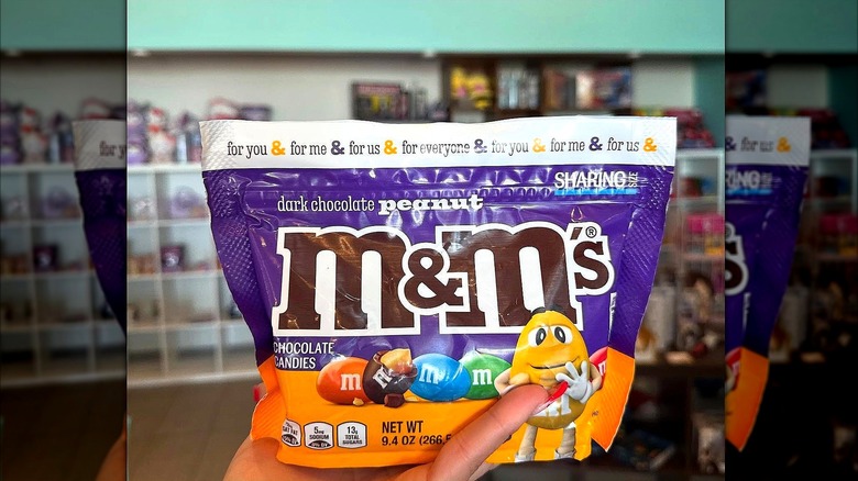Hand holding sharing size bag of Dark Chocolate Peanut M&M's