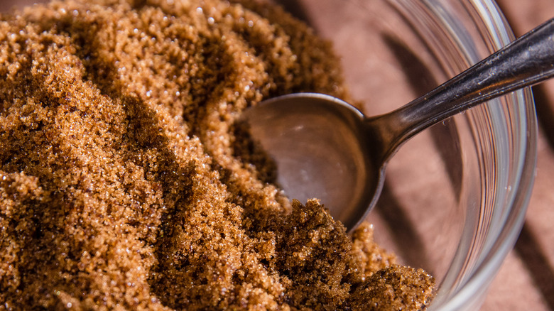 Spoon scooping brown sugar out of a glass bowl