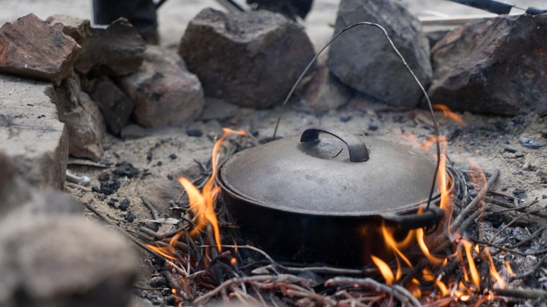 Covered cast-iron pan over a campfire