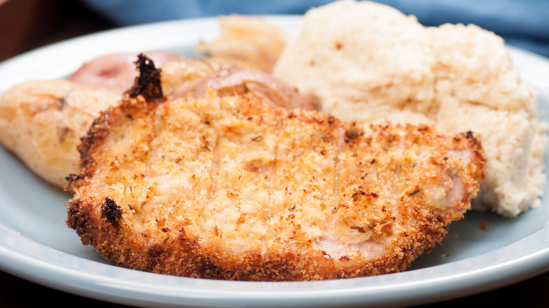 A plate with a breaded pork chop, mashed potatoes, and whole potatoes.