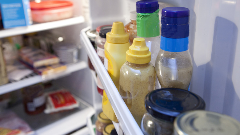 Various condiments on shelf inside an open fridge.