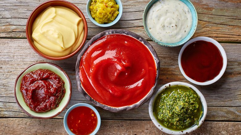 Closeup of various condiments and sauces in small bowls on wood surface.